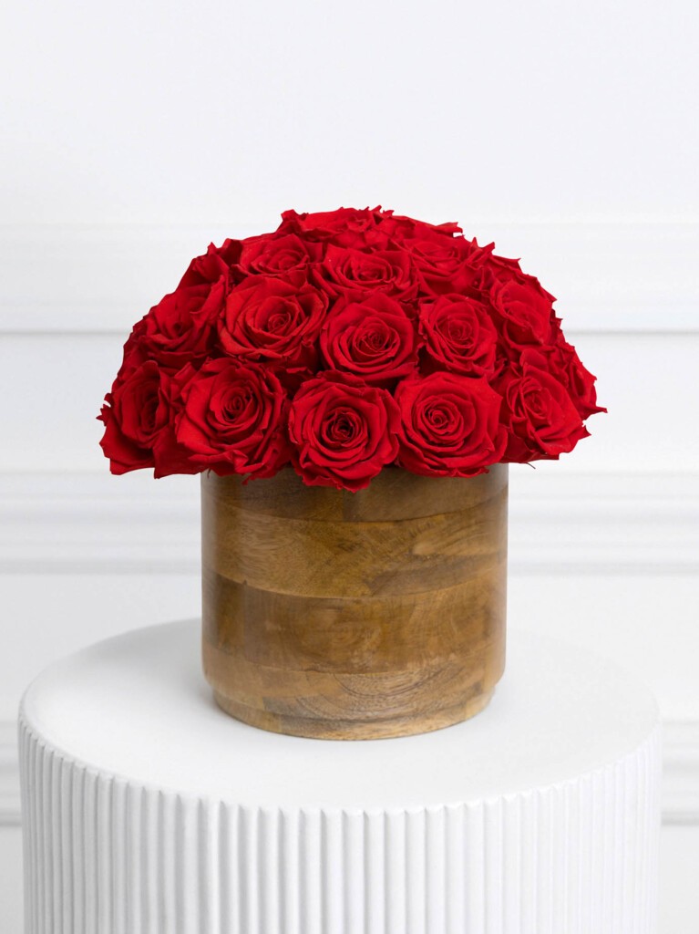 Arrangement of preserved red roses in a perfectly rounded dome, set in a warm, natural wood vase that adds earthy contrast to the rich, velvety blooms for a striking yet timeless display.