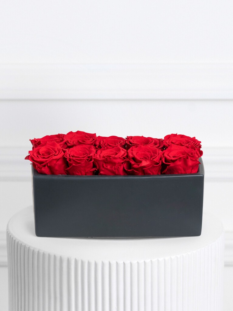 Rectangular black ceramic vase filled with a tight cluster of vivid preserved red roses, creating a bold and luxurious statement with its low-profile, modern silhouette.