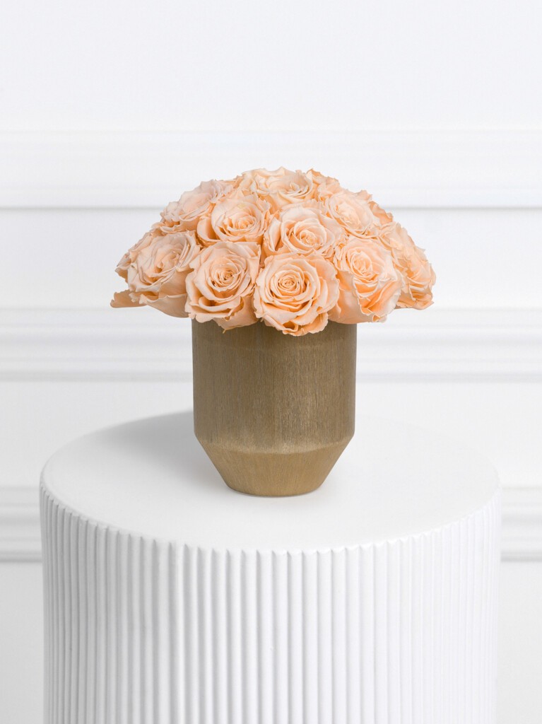 A compact dome of preserved peach roses with softly ruffled petals, elegantly arranged in a faceted matte beige ceramic vase., ideal for celebrations, anniversaries, or housewarming gifts and office arrangements.