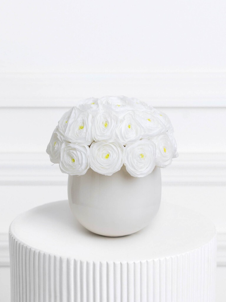 A rounded bouquet of preserved white ranunculus blooms with soft yellow centers arranged in a smooth white vase, offering a minimalist and serene aesthetic.