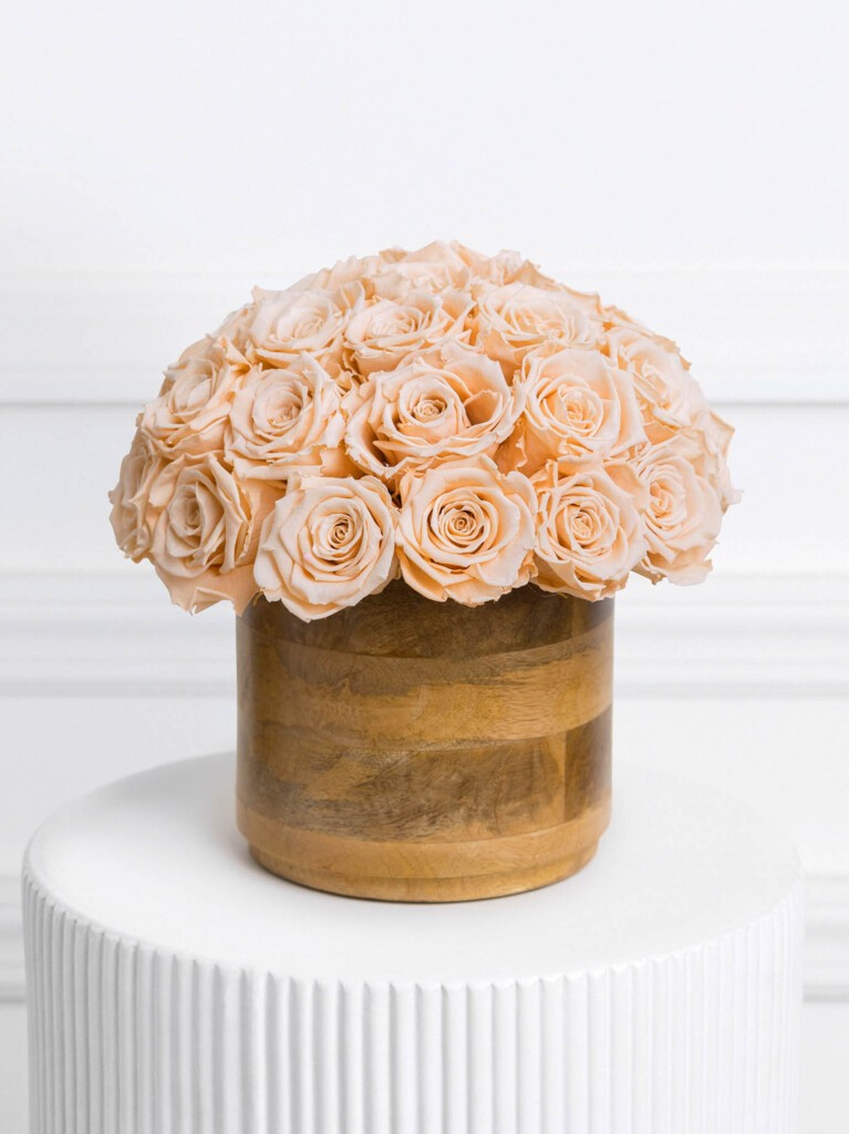 Arrangement of 30 preserved coral-toned roses in a smooth, rounded wooden vase, with tightly clustered blooms forming a soft dome that blends natural warmth with elegant, lasting beauty.