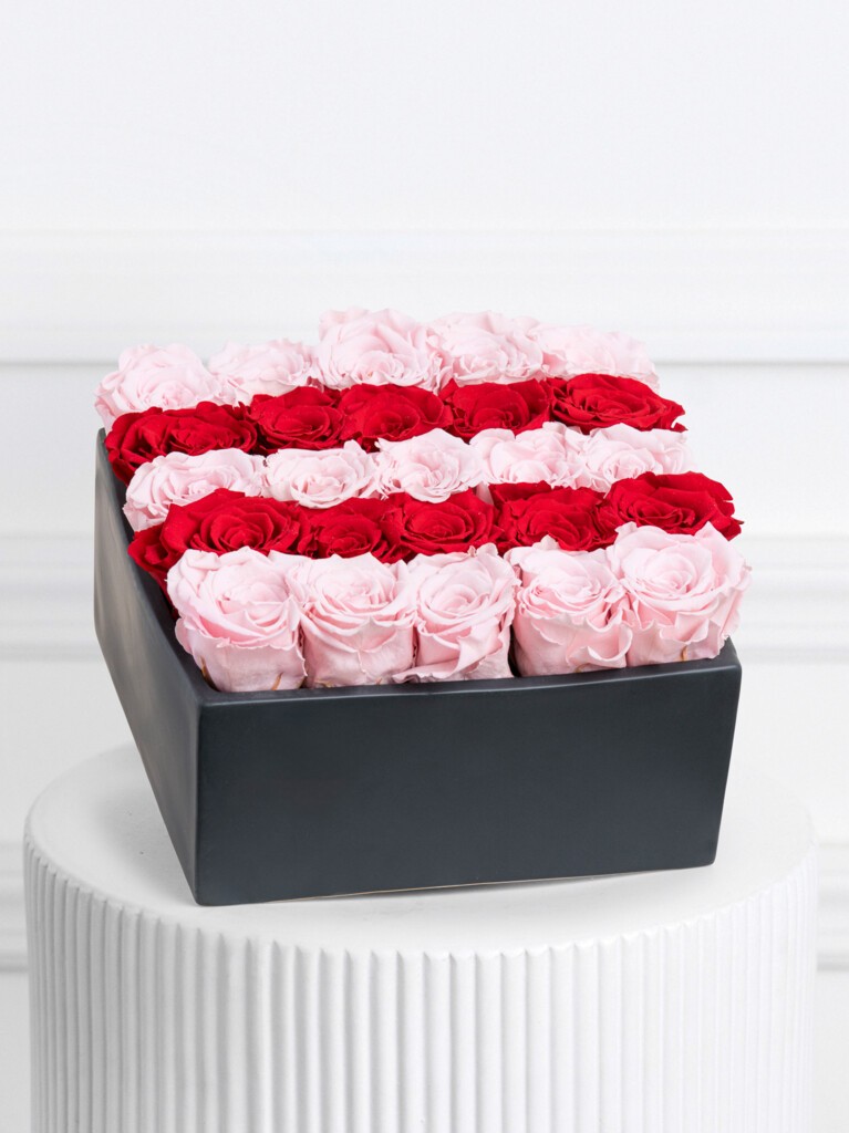 Rectangular black box filled with alternating horizontal rows of preserved pale pink and deep red roses, creating a bold striped color pattern across the entire arrangement.