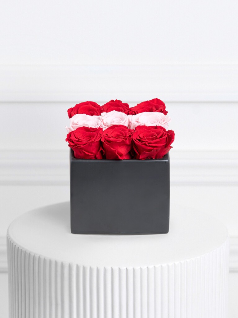 Box arrangement of preserved roses featuring a striking checkerboard pattern of vivid red and soft blush pink blooms, neatly aligned in a matte black square container for a bold, modern presentation.