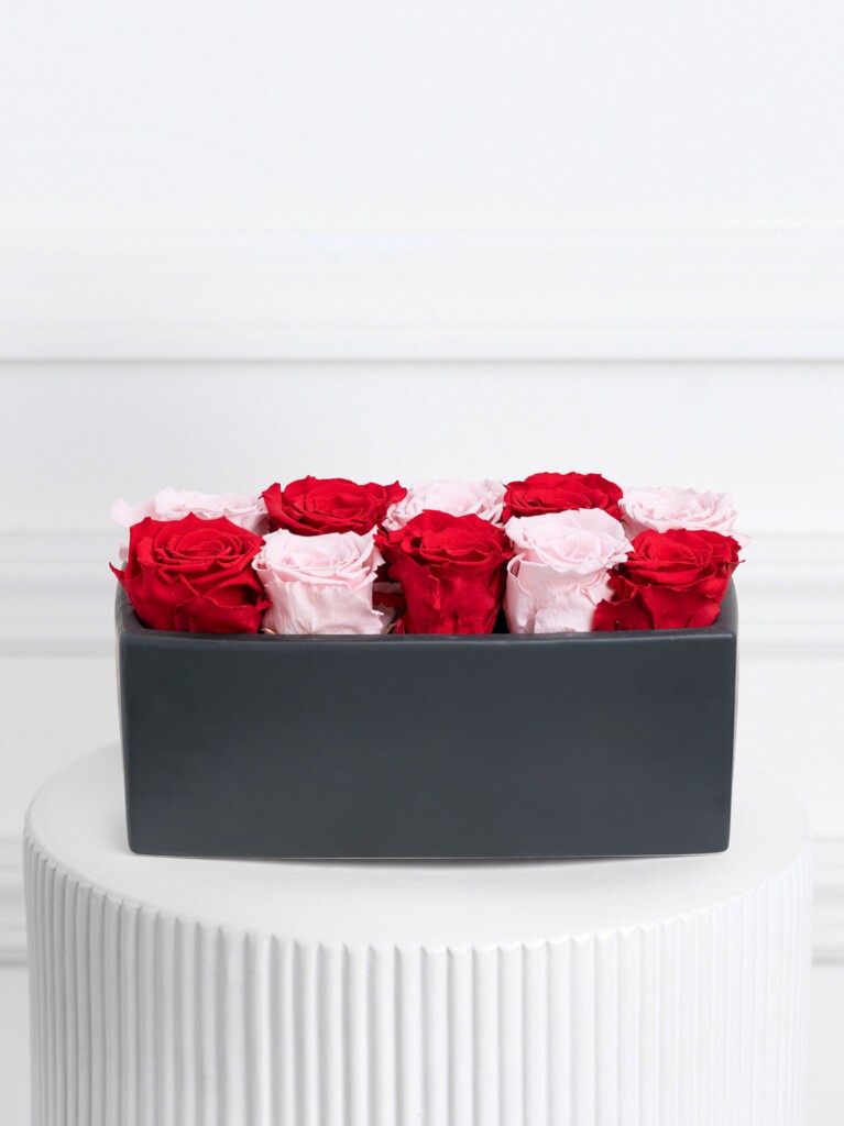 A rectangular black ceramic vase filled with alternating rows of red and light pink preserved roses, neatly aligned in a compact, grid-like pattern for a bold yet refined modern display.