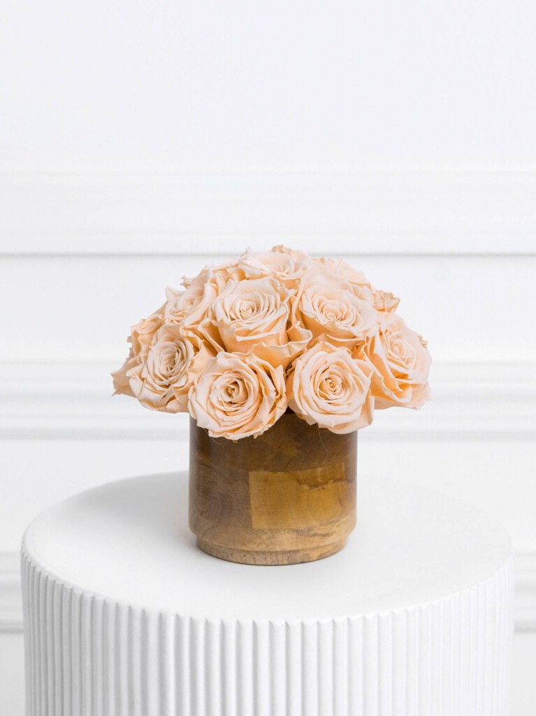 Preserved coral-toned roses arranged in a rounded cluster and displayed in a smooth wooden vase, with soft peach petals and a warm natural base for an elegant, long-lasting centerpiece.
