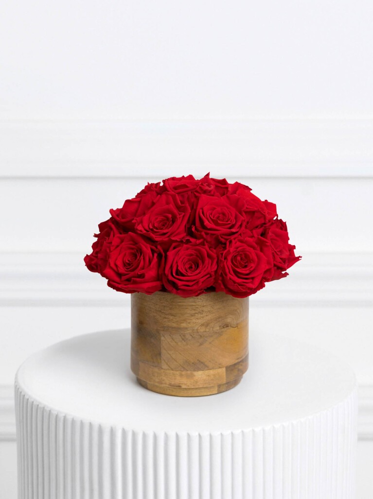 Arrangement of preserved red roses displayed in a natural wood vase, with lush, velvety blooms arranged in a rounded cluster for a bold and timeless floral statement.