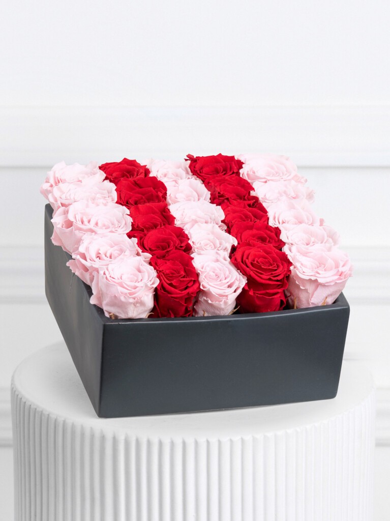 Rectangular black box filled with alternating horizontal rows of preserved pale pink and deep red roses, creating a bold striped color pattern across the entire arrangement.